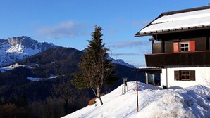 Ein zweistöckiges Gebäude mit schneebedecktem Dach und Bergelandschaft im Hintergrund.