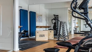 Ein Heimfitnessraum mit Laufband, Gewichtecke und verschiedenen Trainingsgeräten.