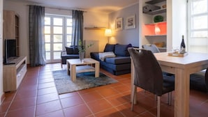 Ein modernes Wohnzimmer mit einer Couch, einem Couchtisch, einem Esstisch mit Stühlen, einem Fernseher und einem Fenster mit Vorhängen.