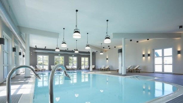 Ein Hallenbad mit klarem Wasser, umgeben von Liegestühlen und Sonnenliegen.