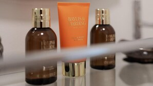 A bathroom with a mirror, a sink, and three bottles of Baylis & Harding products.