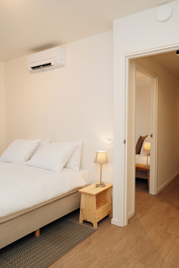 A bedroom with a bed, bedside table, lamp, and an air conditioning unit.