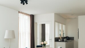 A modern hotel room with a sofa, dining table, chairs, and a kitchenette. - Urban Suites (Eindhoven)