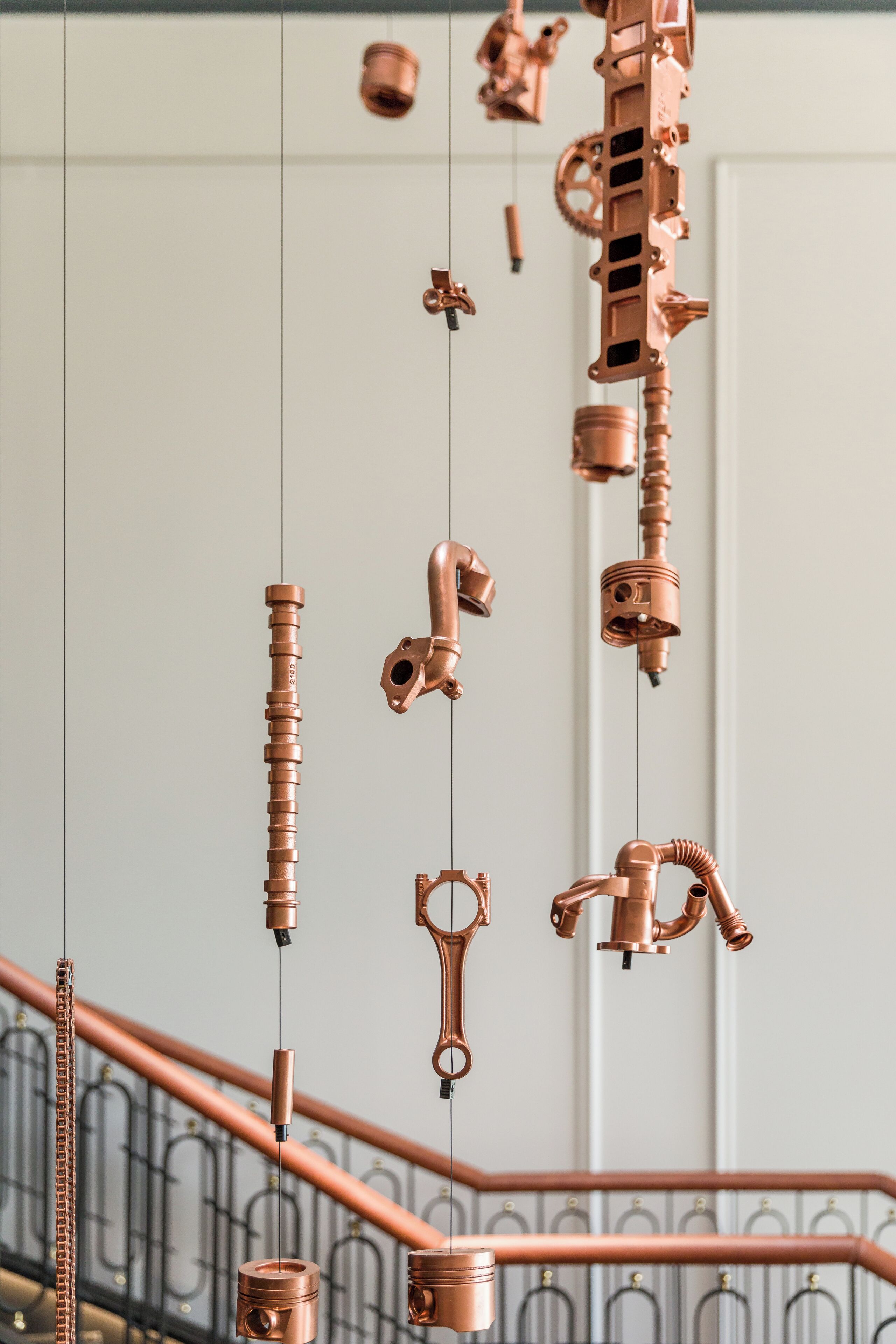 A staircase with a metal railing and a series of hanging copper pipes and fittings.