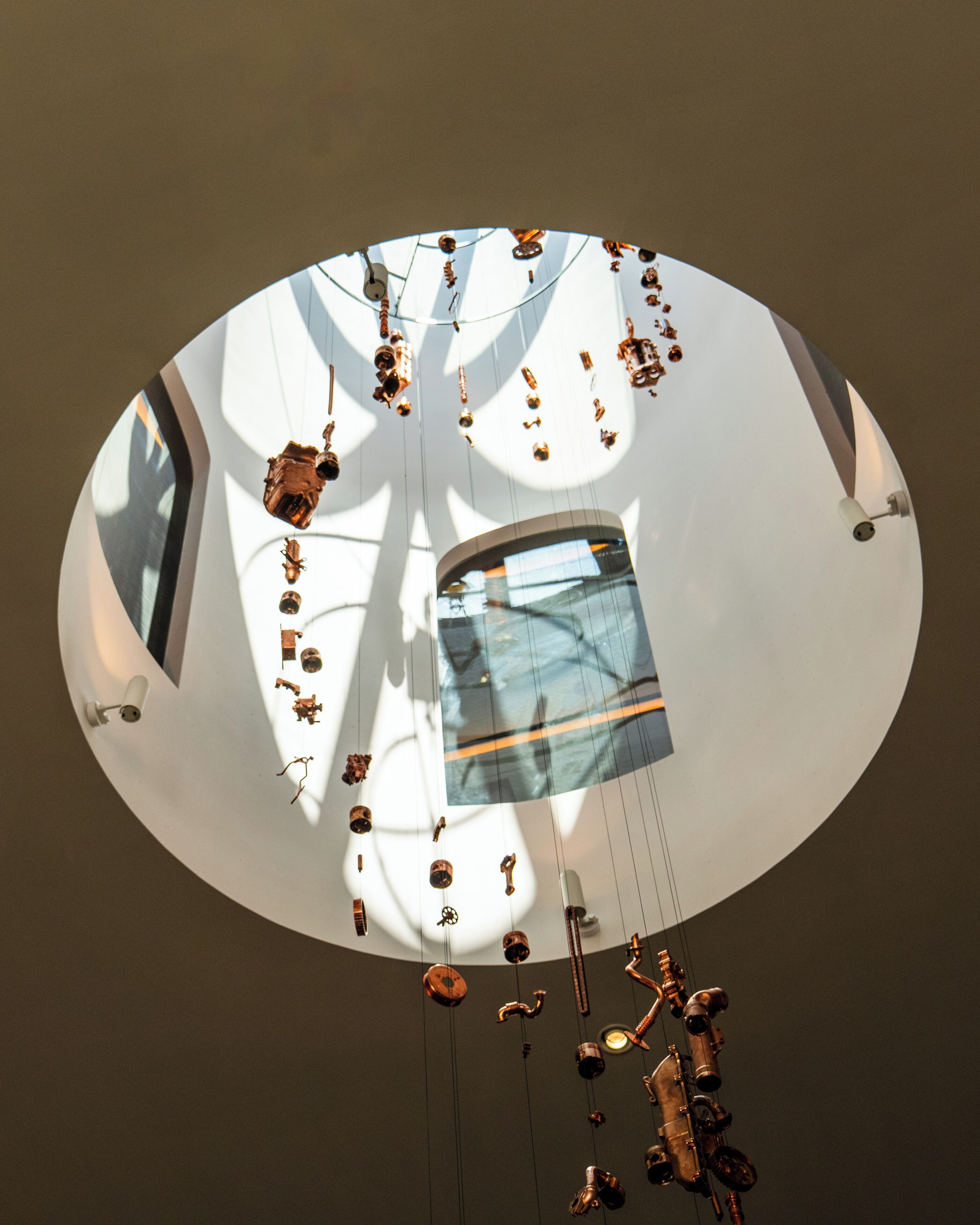 Techo circular con varios objetos colgantes y una ventana que refleja el cielo.