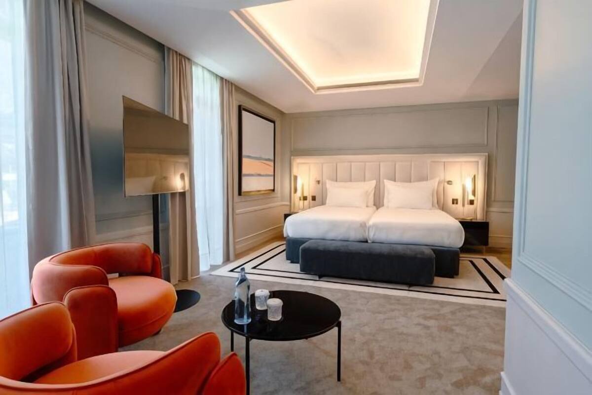 Een hotelkamer met een bed, een bureau, twee stoelen, een televisie en een groot raam.