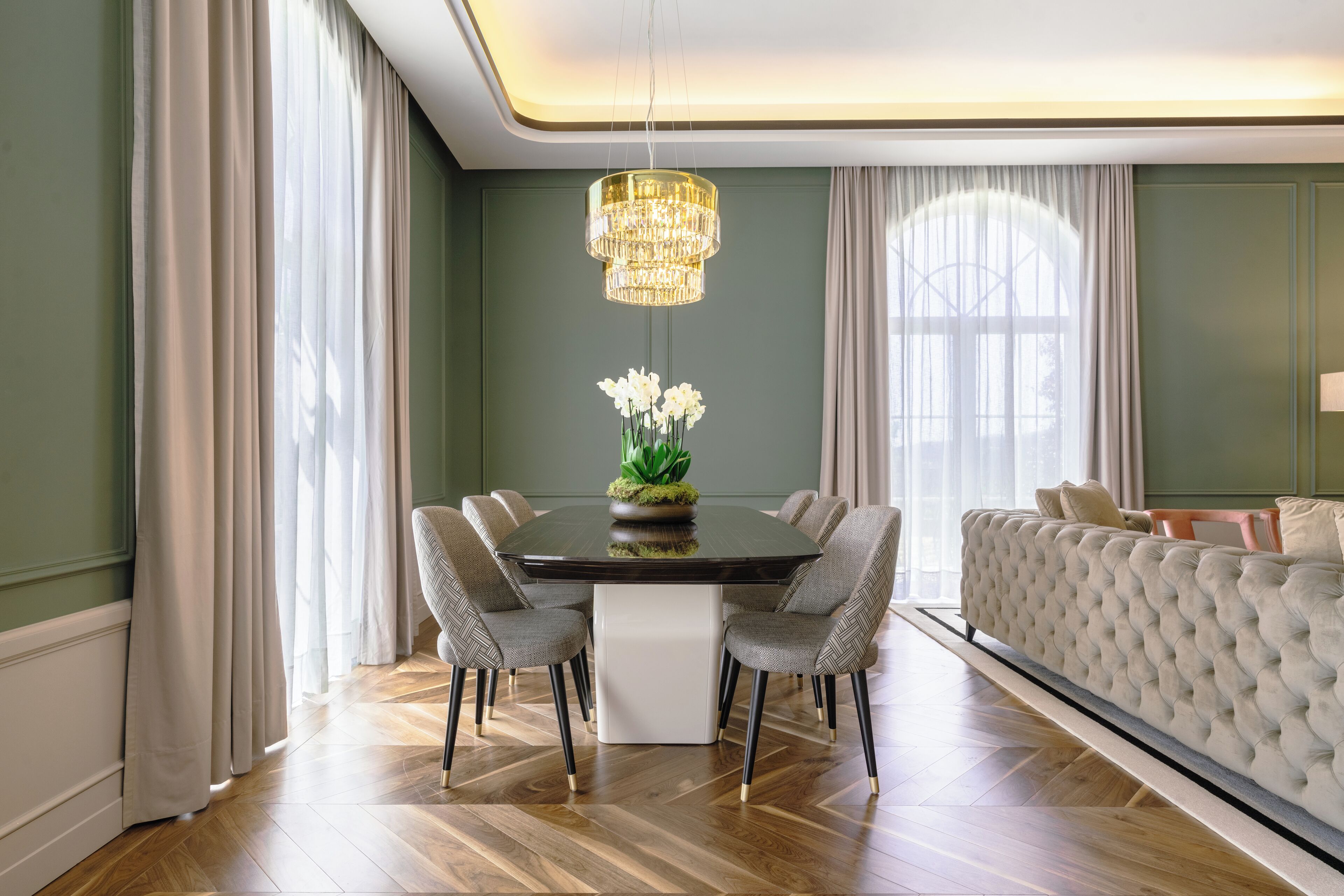 Uma sala de jantar com uma mesa redonda, seis cadeiras, um candelabro e um sofá.