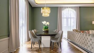 Uma sala de jantar com uma mesa redonda, seis cadeiras, um candelabro e um sofá.