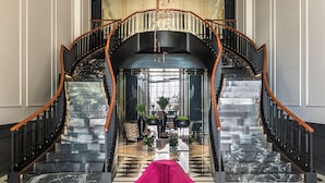 A grand staircase with a black and white marble floor, a pink chair in the foreground, and a chandelier above. - Amoure Hotel (Vila Verde)
