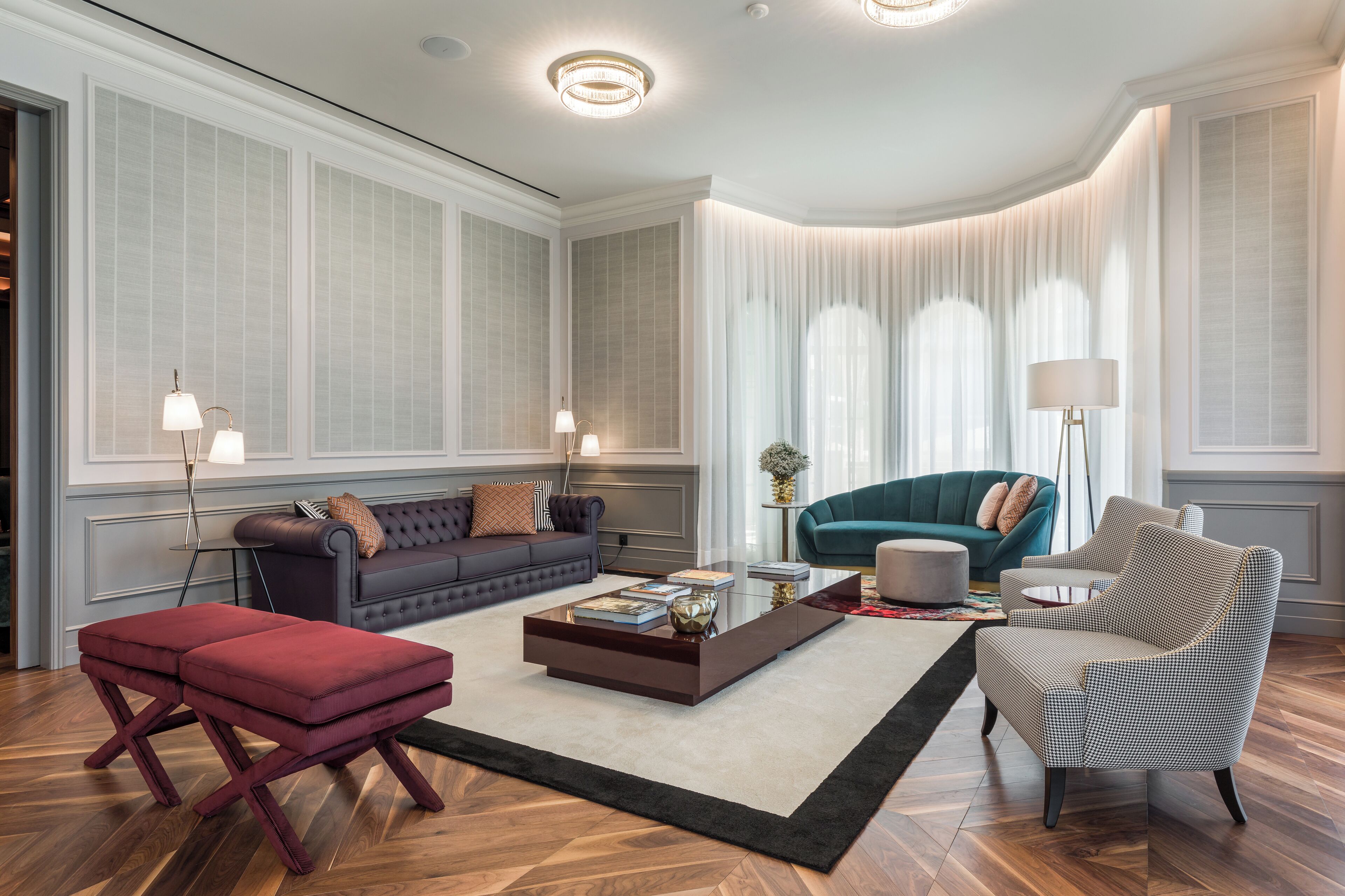 A modern living room with a dark sofa, a red ottoman, a patterned armchair, and a coffee table.
