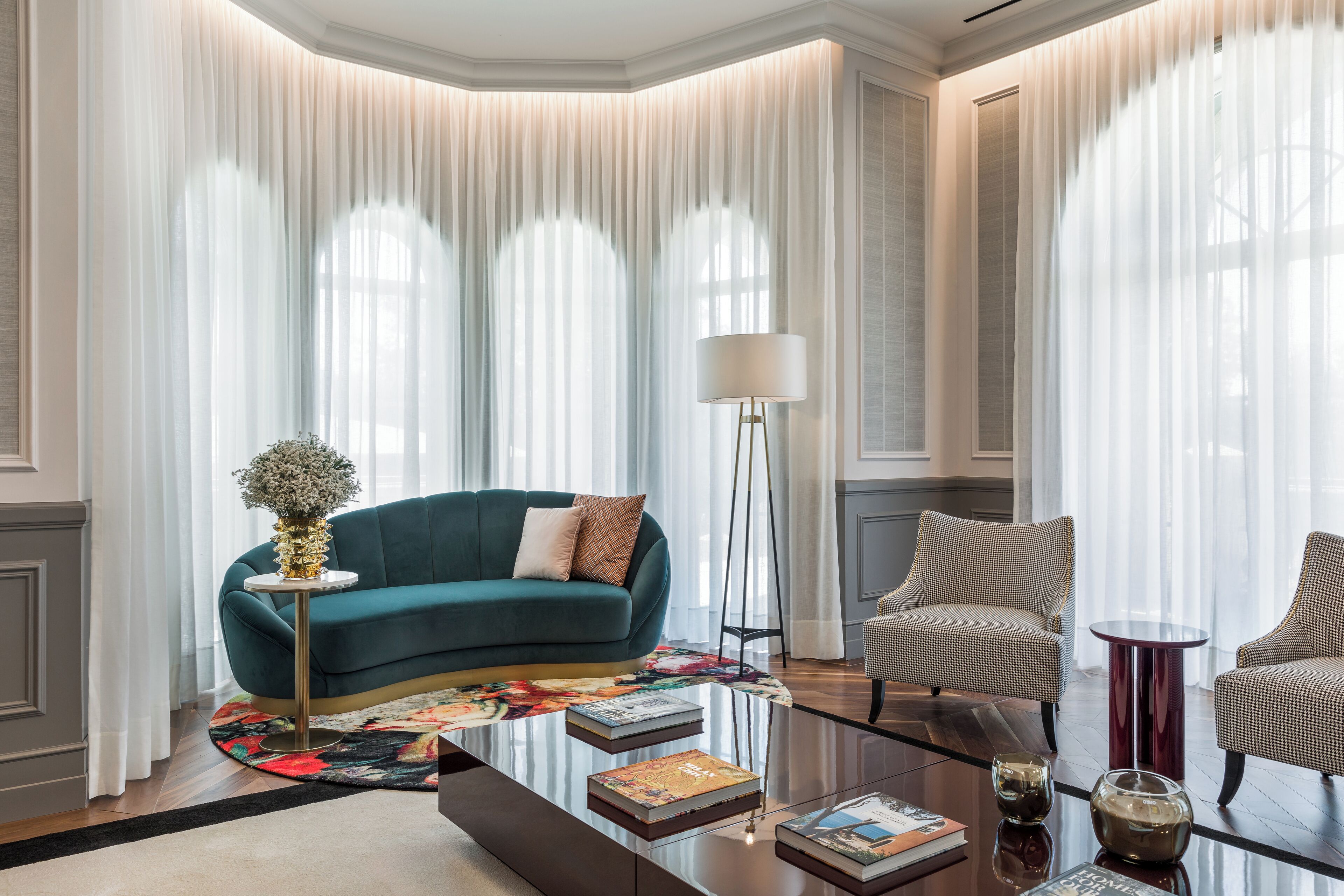 A modern living room with a teal sofa, a round coffee table, and two armchairs.