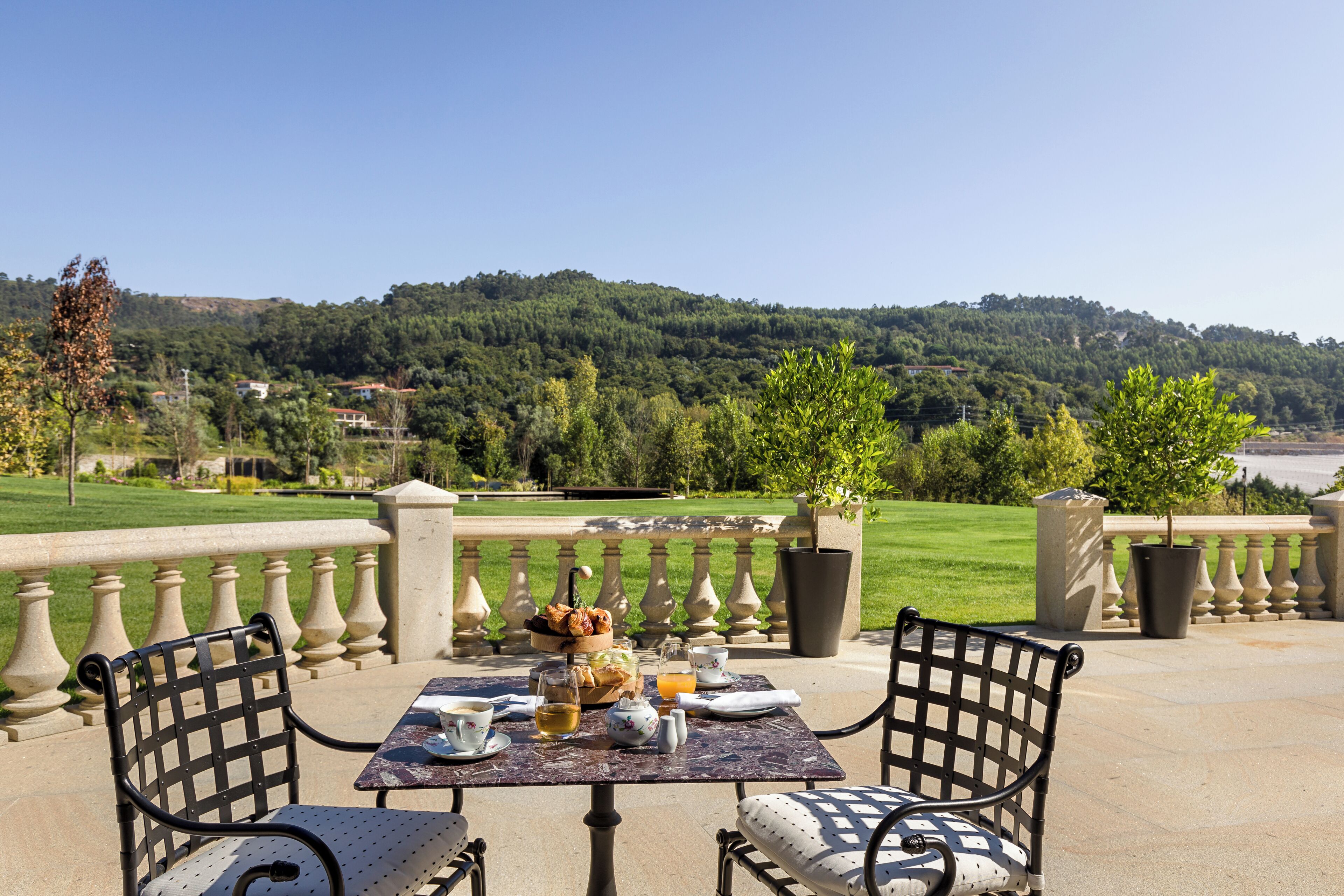 An outdoor dining area with a table set for two, overlooking a scenic hillside.