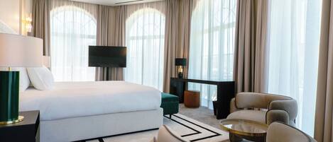 A modern hotel room with a bed, a TV, a desk, a chair, and a sofa.