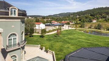 A large building with a green facade, a courtyard with a lawn, and a view of a hilly landscape in the background.