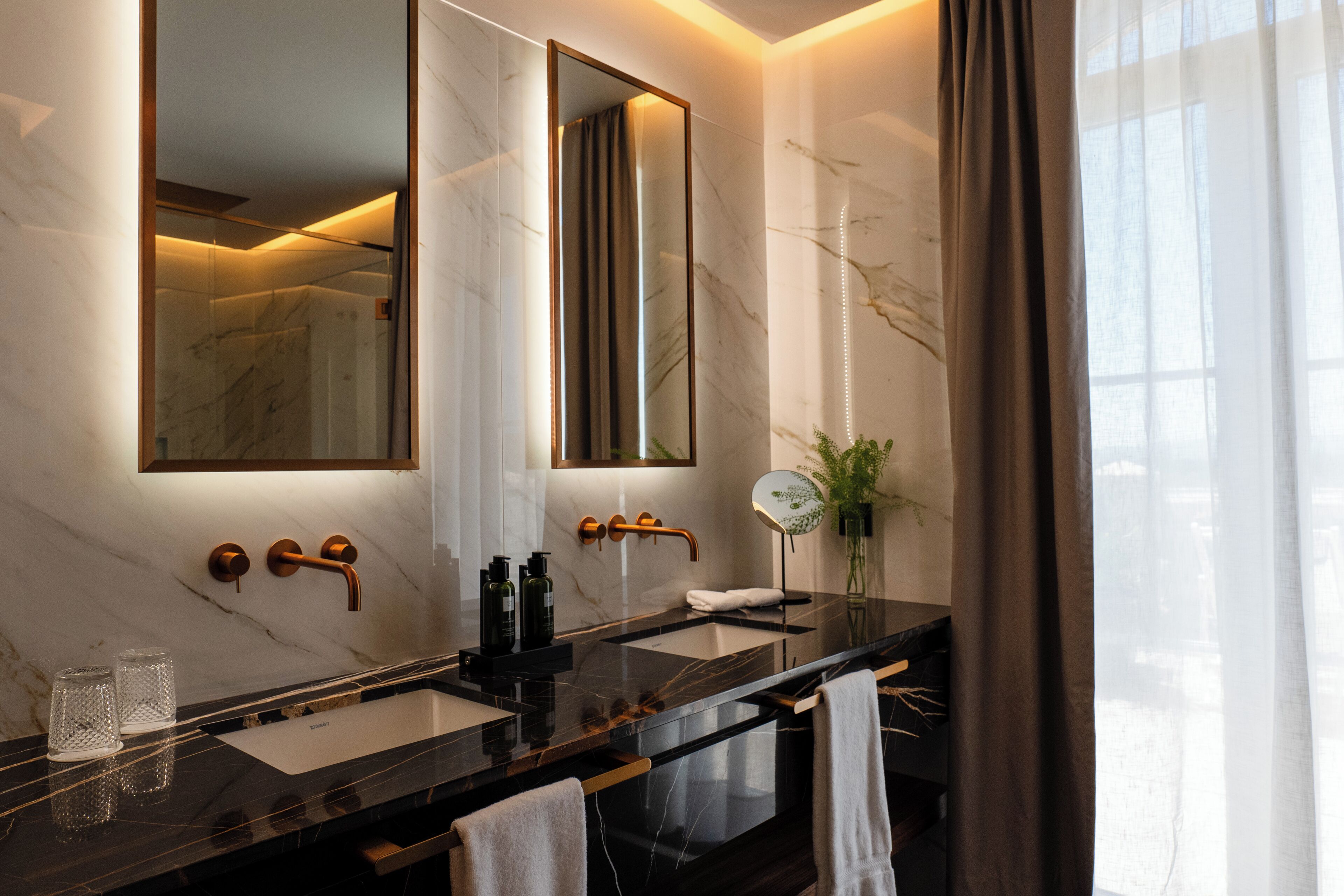 Une salle de bain moderne avec deux lavabos, un grand miroir et une plante.