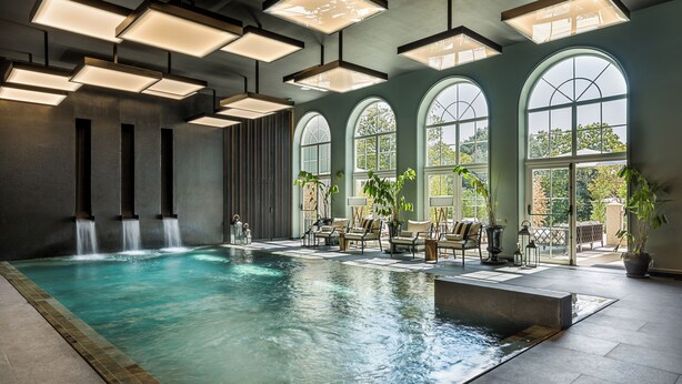 A spacious indoor swimming pool with multiple seating areas and large arched windows. - Amoure Hotel (Vila Verde)