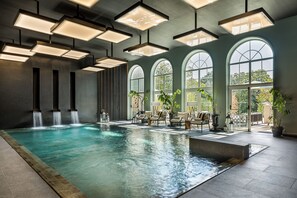 Una amplia piscina cubierta con varias zonas de descanso y grandes ventanales en arco.