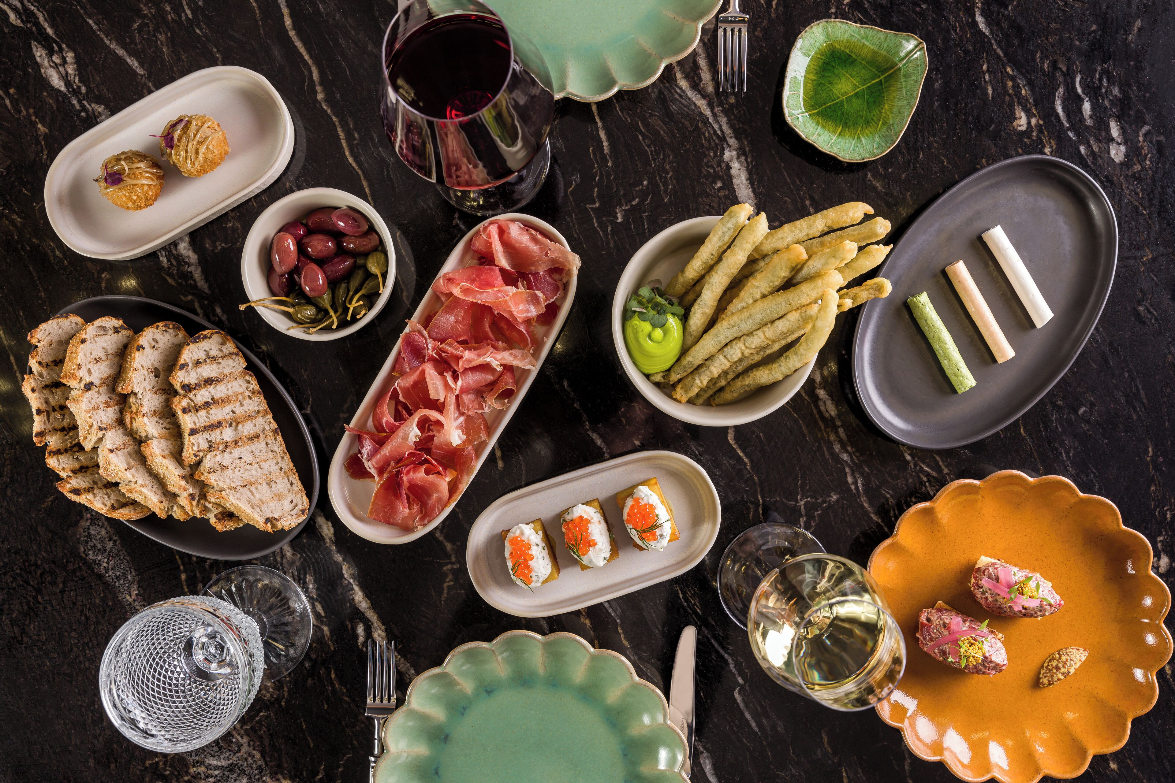 A variety of food items and dishes arranged on a dark marble table.