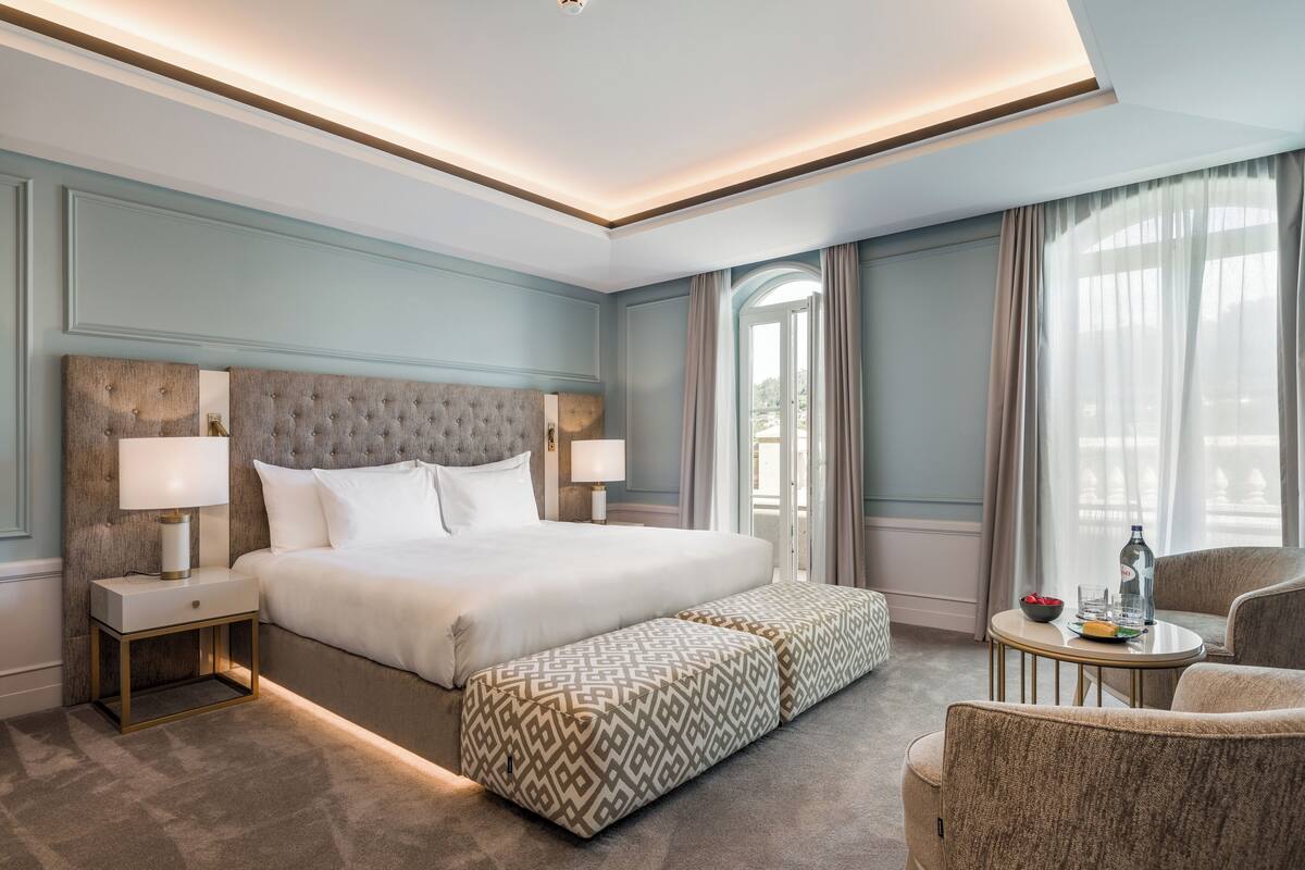 Een hotelkamer met een groot bed, nachtlampjes, een tafeltje met een fles en een stoel.