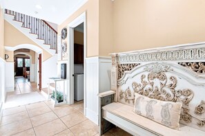 A spacious interior with a staircase leading to a second floor, a cozy seating area with a decorative headboard, and a kitchen visible through an open doorway.