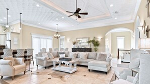 A spacious living room with a high ceiling, a ceiling fan, and a fireplace. There are multiple seating areas with sofas and armchairs. - Waterfront Home w/ Pool, Boat Slip & Private Beach Access – Holiday Isle (Destin)