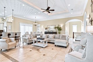 Un soggiorno spazioso con soffitto alto, ventilatore a soffitto e camino. Sono presenti diverse zone relax con divani e poltrone.