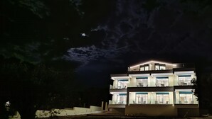 A multi-story building with illuminated windows and a balcony, surrounded by trees. - AIR IN ROOMS (Spata-Artemida)