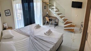 A hotel room with a large bed, a desk, a chair, a staircase, and a TV on the wall. - AIR IN ROOMS (Spata-Artemida)