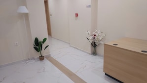 A hotel reception area with a marble floor, a reception desk, a potted plant, a standing lamp, and a vase of flowers. - AIR IN ROOMS (Spata-Artemida)