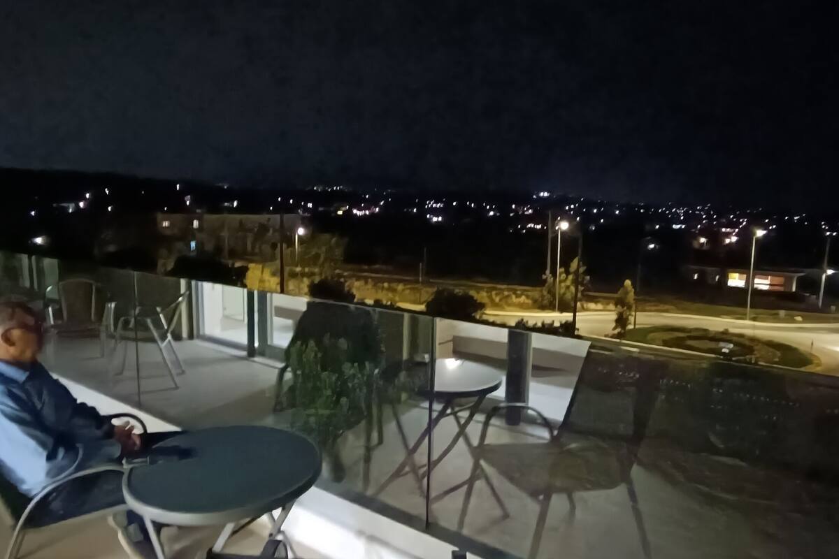 A balcony with a table and chairs, overlooking a cityscape at night.