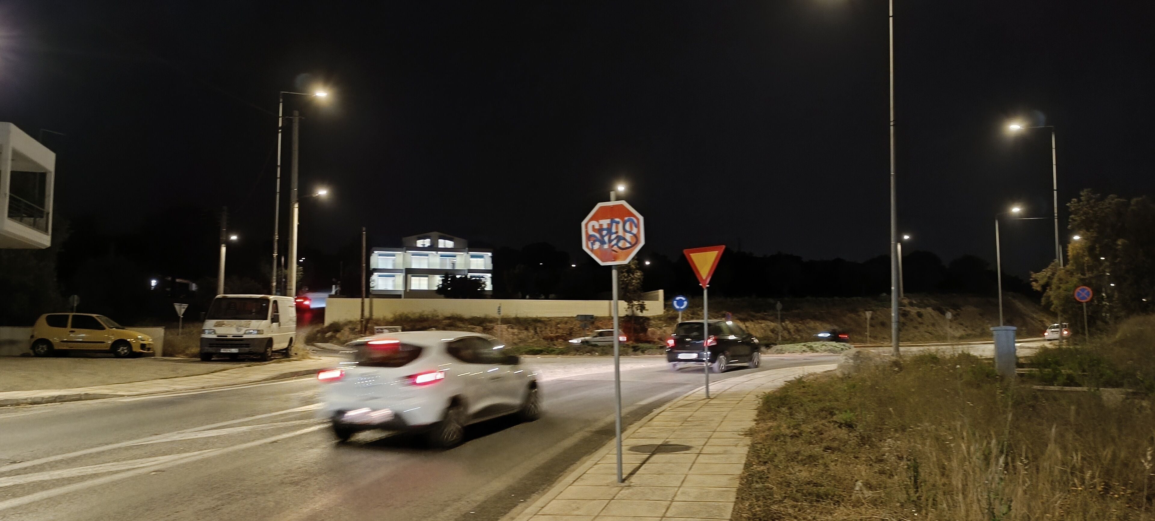 A nighttime street scene with cars, streetlights, and road signs.
