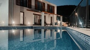 Un edificio moderno con piscina, ventanas amplias y mobiliario exterior.