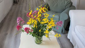A living room with a green sofa, a white couch, and a vase of flowers on a white table. A staircase is visible in the background leading to a kitchen area. - Maison de La Porte des Loups au Pied du Ventoux à Ste Colombe (Bédoin)