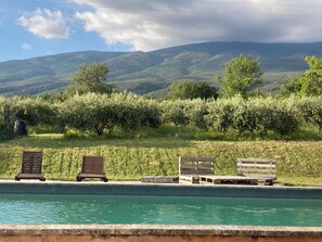 Una piscina con tumbonas de madera y vistas a un paisaje montañoso.