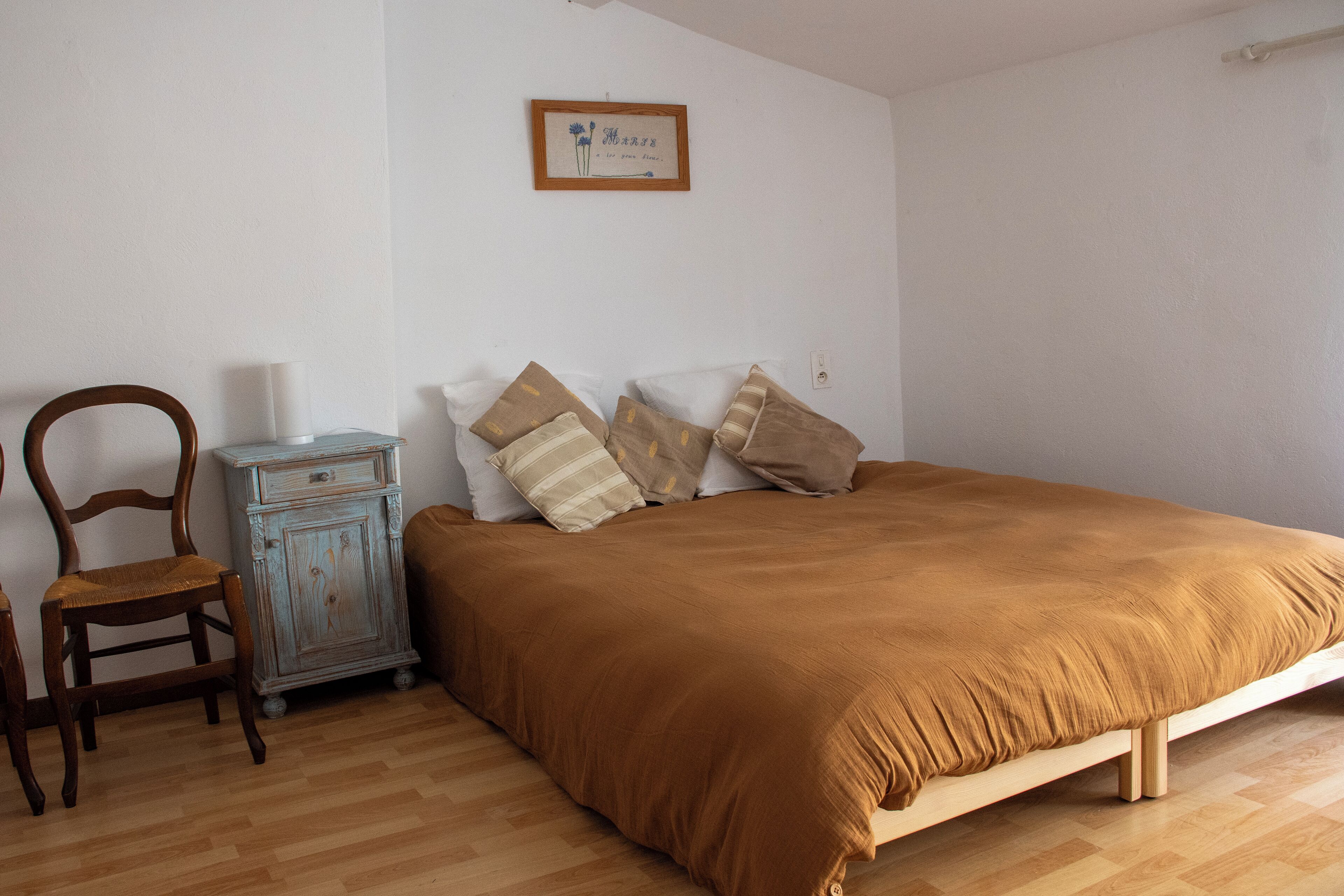A bedroom with a wooden bed, a chair, a small dresser, and a framed picture on the wall.