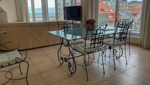 Een eethoek met een glazen tafel en metalen stoelen, een bank en een televisie aan de muur.