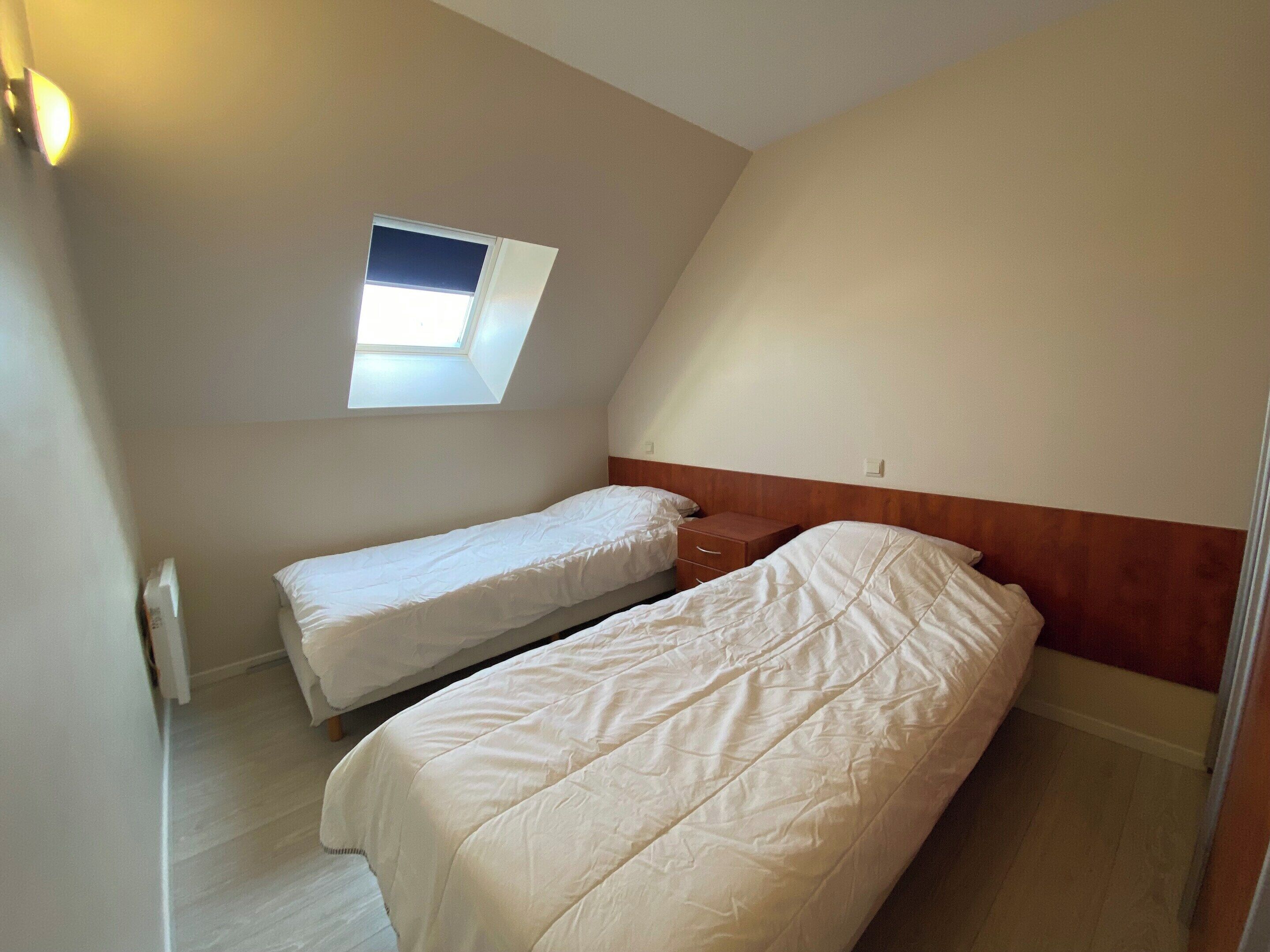 Een kleine kamer met twee bedden, een dakraam en een houten hoofdbord.