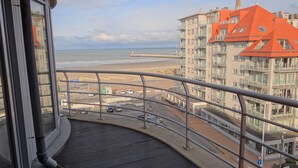 Een balkon met uitzicht op een strand, een steiger en een meerhoog gebouw met oranje daken.