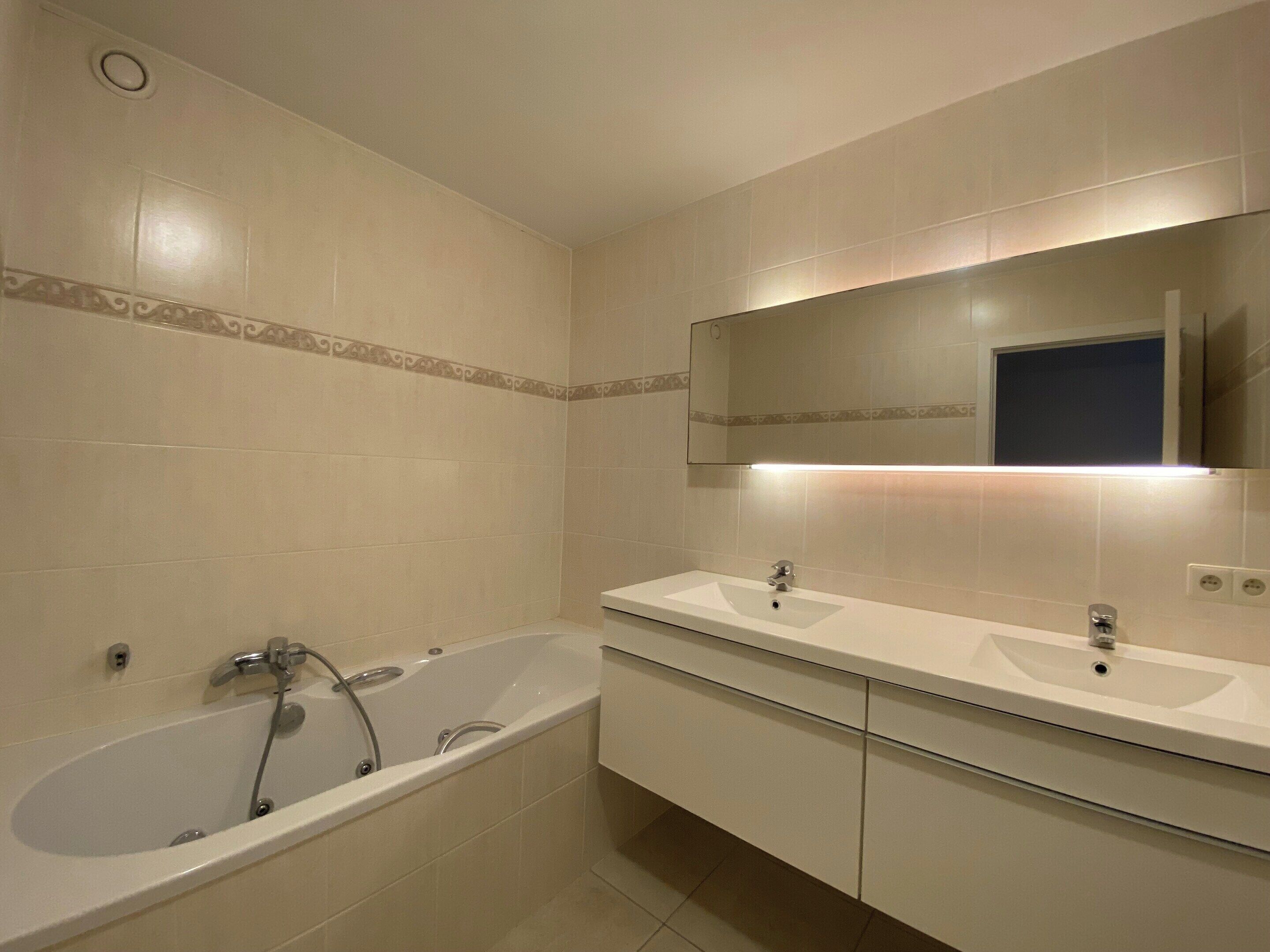 A modern bathroom with a bathtub, two sinks, and a large mirror.