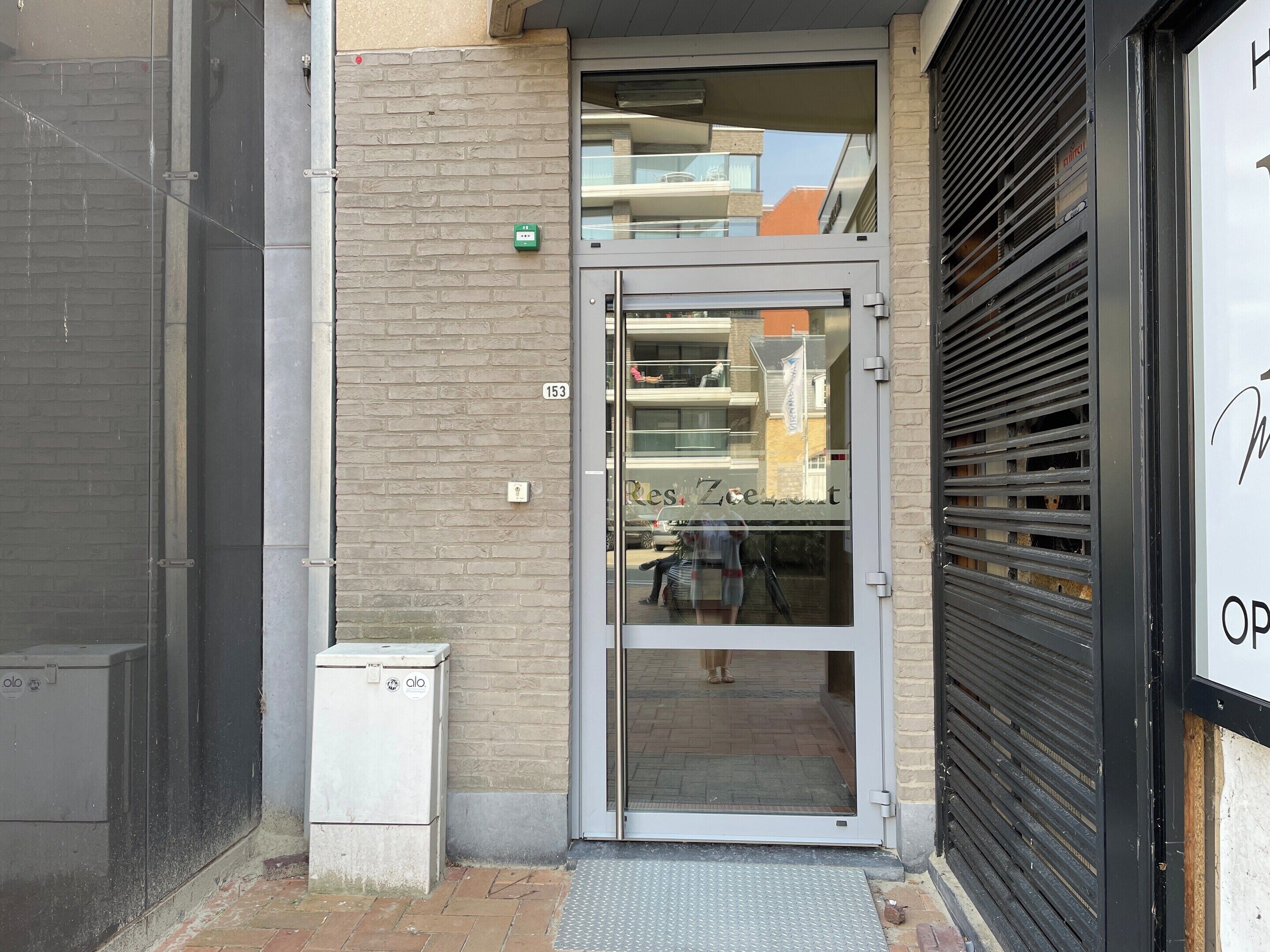 Une entrée d’immeuble avec une porte en verre, un mur en briques et un portail en métal.