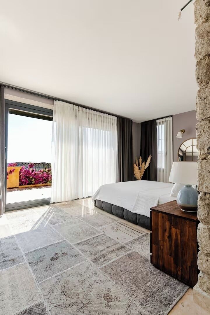 Un dormitorio moderno con una cama grande, una mesita de noche de madera, una lámpara y vistas a flores a través de una puerta corrediza.