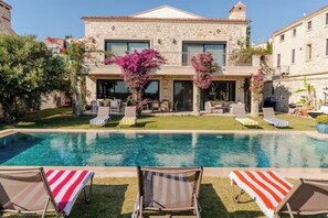 A stone villa with a swimming pool, outdoor seating, and lush greenery.