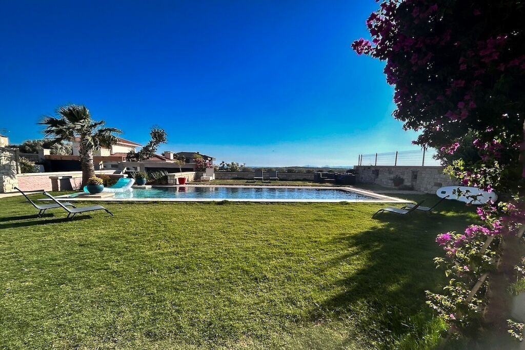 A swimming pool with lounge chairs, a grassy lawn, and a clear blue sky.