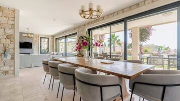 A spacious dining area with a long table and chairs, a chandelier, and a view of the outdoors.