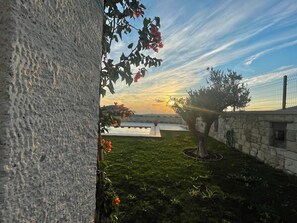 Een binnentuin met een stenen muur, een boom en een uitzicht op de zonsondergang boven het water.