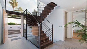 A modern interior with a glass staircase leading to a balcony, a minimalist design, and a view of palm trees. - Villa O2 - beautiful property in Alcudia (Alcudia)