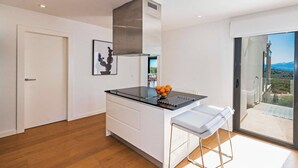 A modern kitchen with a black countertop, stainless steel range hood, and a bowl of oranges. There is a white bench and a door to the left. - Villa Panoramica - modern villa in Alcudia (Alcudia)