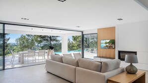 A modern living room with a beige sofa, a wooden side table, and a TV mounted on the wall. - Villa Sky - private swimming pool and terrace (Alcudia)