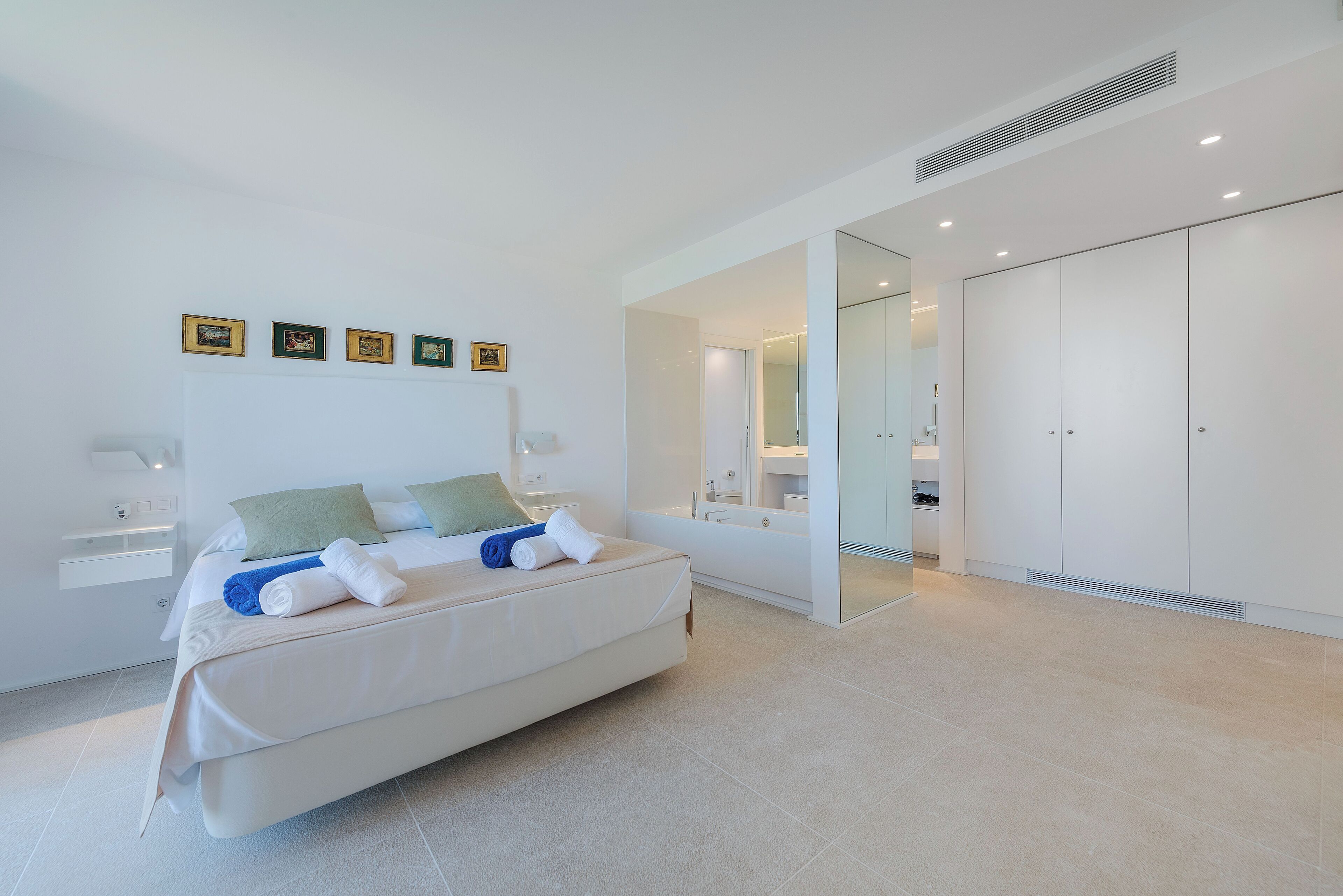 A modern bedroom with a large bed, a walk-in closet, and a bathroom visible through an open door.
