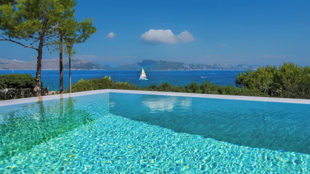 Ein klares, blaues Schwimmbecken mit Blick auf das Meer und die dahinterliegenden Berge.